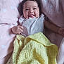 baby, smiling, tongue_out, blanket, yellow_blanket, pink_blanket, heart_pattern, curly_hair, infant, happy, cozy, cute, lying_down, soft_texture, indoors, child, clothing, portrait, toddler, playful