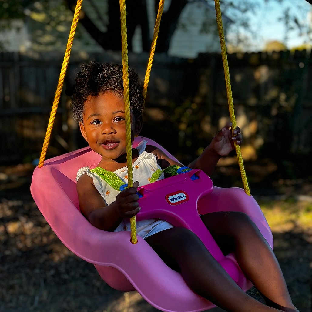 Skylar is registered to the contest to win money with this photo: child, face, female, girl, grass, happy, head, nature, outdoorplayarea, outdoors, park, person, photography, plant, play, playarea, portrait, sitting, swing, toy