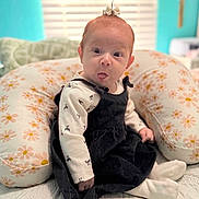 Haislyn is registered to the contest to win money with this photo: baby, child, tongue_out, bow, pillow, floral_pattern, black_dress, white_shirt, socks, indoor, cute, playful, portrait, infant, seated, soft_light, home, expression, small_hands, cozy