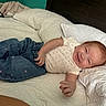 Haislyn is registered to the contest to win money with this photo: baby, child, smiling, bed, pillow, blue_pants, white_bedspread, indoor, clothing, cute, happy, person, infant, portrait, head, hand, fabric, room, home, relaxing