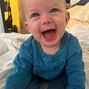 Vincent joined the competition — help win amazing prizes! baby, child, smiling, blue_sweater, bed, blanket, indoor, happy, person, infant, cute, laughing, clothing, face, head, human, sitting, warm_light, cozy, room