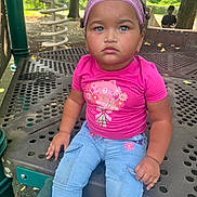 Jana is registered to the contest to win money with this photo: child, toddler, playground, pink_shirt, blue_jeans, headband, curly_hair, outdoor, park, play_equipment, metal_structure, serious_expression, sitting, daylight, trees, greenery, cute, young_child, casual_clothing, person