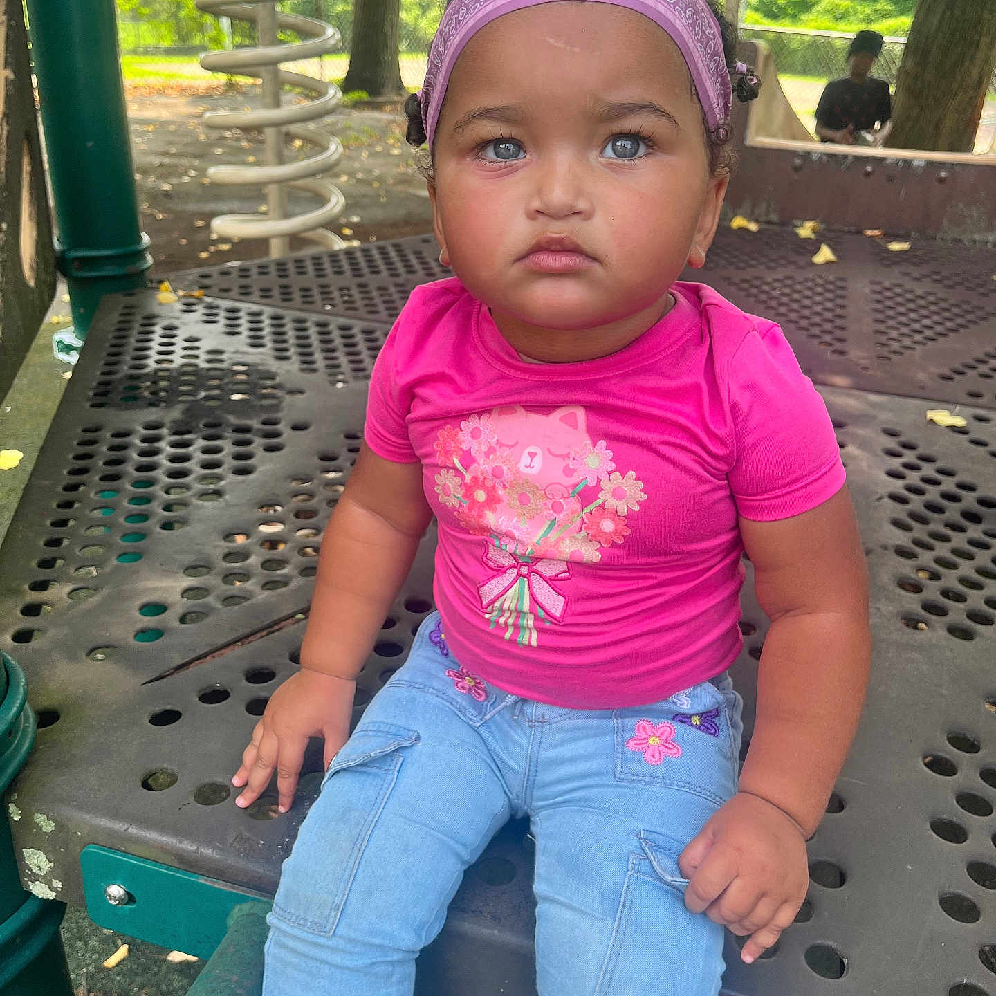 Jana is registered to the contest to win money with this photo: child, toddler, playground, pink_shirt, blue_jeans, headband, curly_hair, outdoor, park, play_equipment, metal_structure, serious_expression, sitting, daylight, trees, greenery, cute, young_child, casual_clothing, person