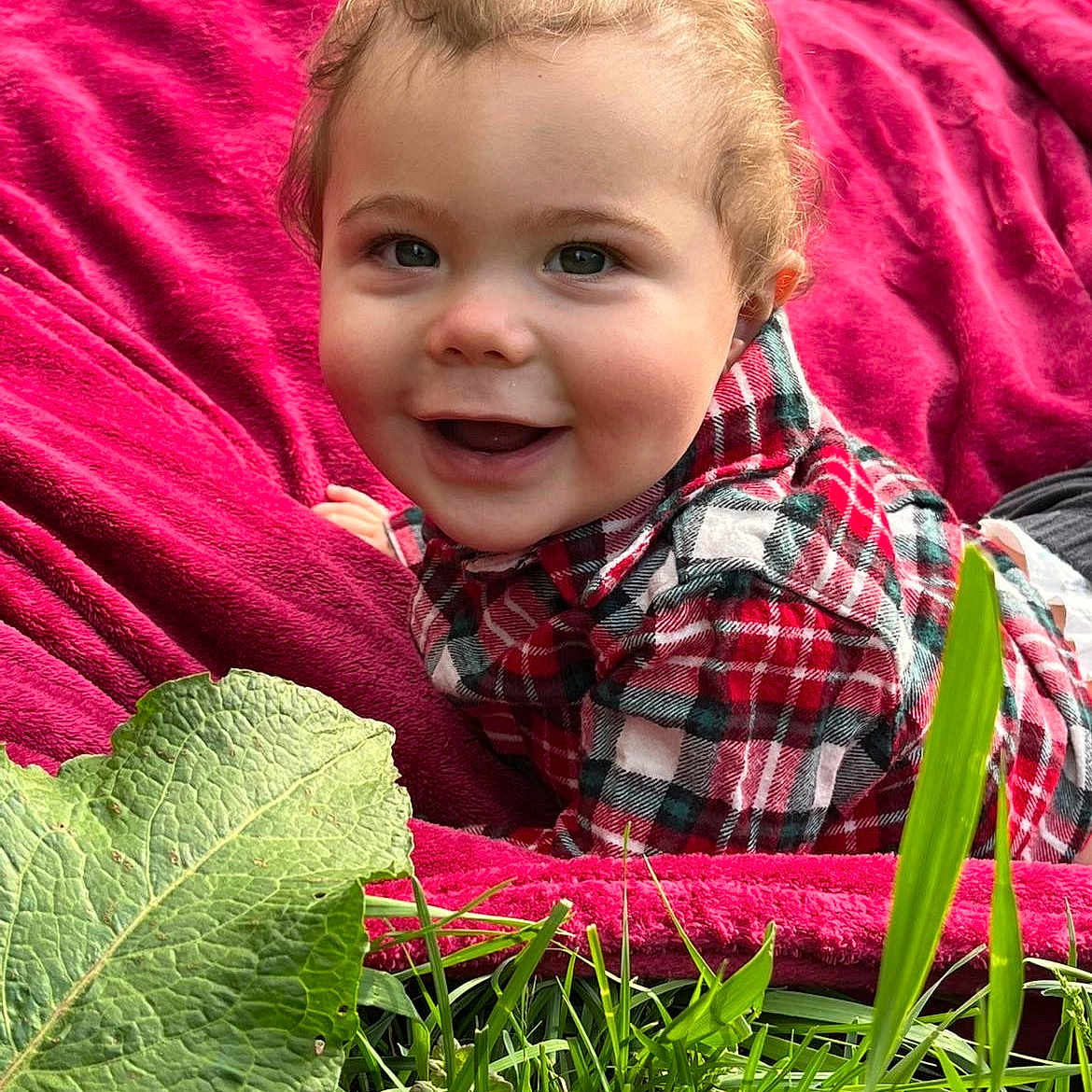 Devon is registered to the contest to win money with this photo: baby, blanket, face, grass, green, happy, head, herbal, herbs, leaf, nature, outdoors, park, person, photography, plant, portrait, pottedplant, quilt, smile