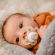 Amari joined the competition — help win amazing prizes! baby, infant, pacifier, blanket, cozy, close_up, blue_eyes, portrait, lying_down, soft_texture, fur_blanket, hand, newborn, clothing, warm_tone, skin, face, gaze, soft_lighting, eye_contact