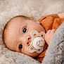 baby, infant, pacifier, blanket, cozy, close_up, blue_eyes, portrait, lying_down, soft_texture, fur_blanket, hand, newborn, clothing, warm_tone, skin, face, gaze, soft_lighting, eye_contact