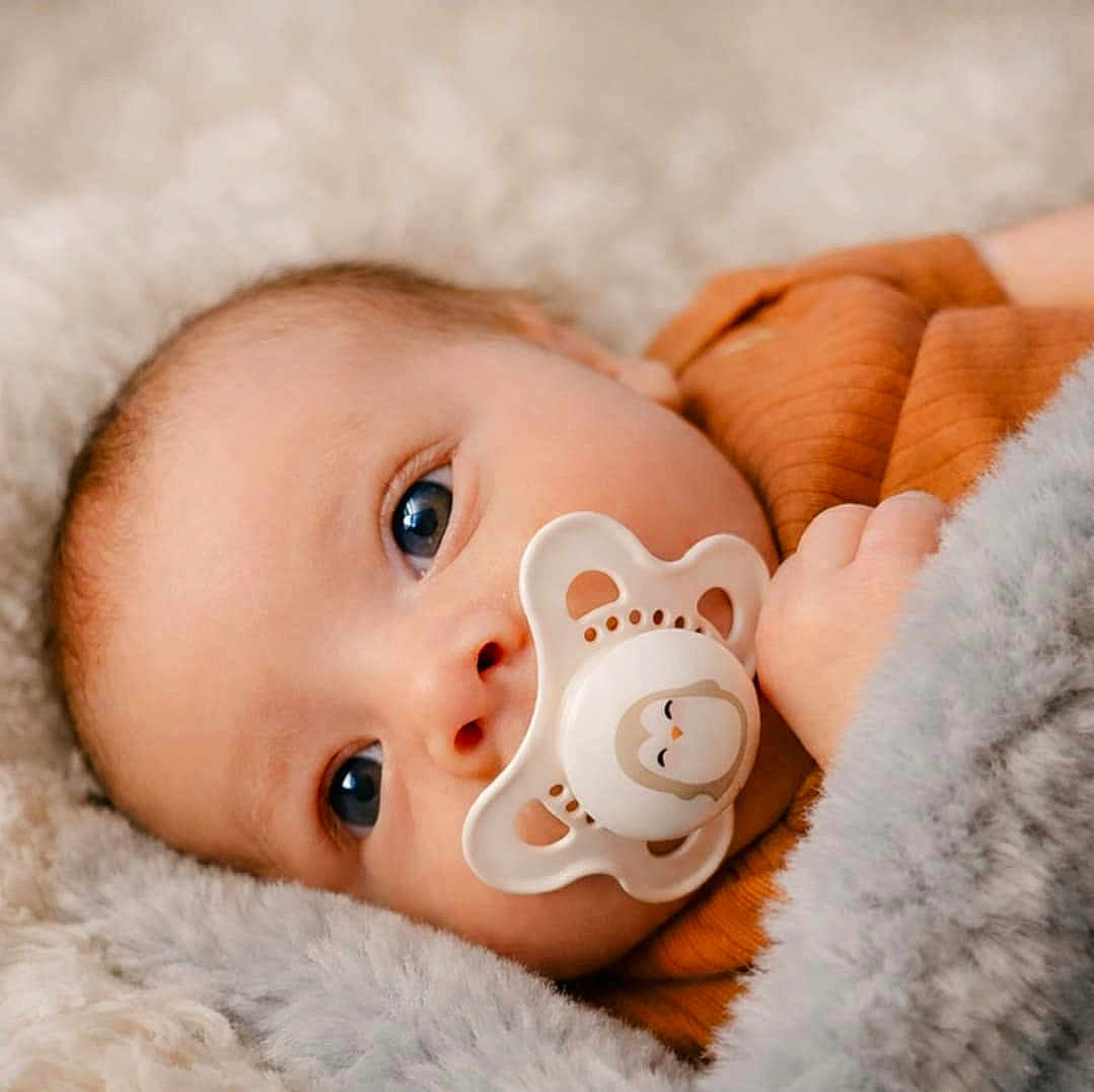 Amari joined the competition — help win amazing prizes! baby, infant, pacifier, blanket, cozy, close_up, blue_eyes, portrait, lying_down, soft_texture, fur_blanket, hand, newborn, clothing, warm_tone, skin, face, gaze, soft_lighting, eye_contact