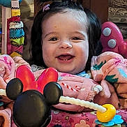 Scarlett joined the competition — help win amazing prizes! baby, child, smiling, indoor, toy, pink_clothing, minnie_mouse, activity_center, face, happy, young_child, play, colorful, cute, person, seated, hair_tie, wood_background, closeup, infant