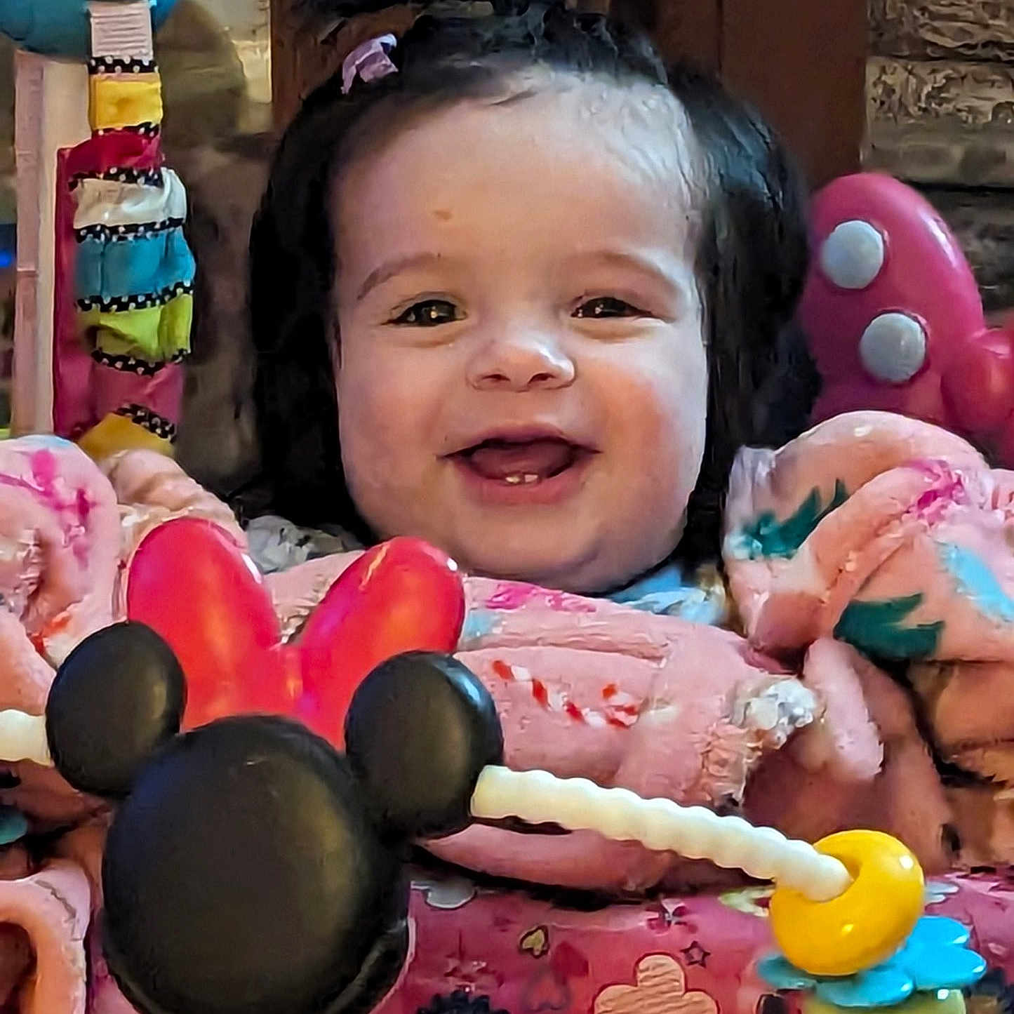 Scarlett joined the competition — help win amazing prizes! baby, child, smiling, indoor, toy, pink_clothing, minnie_mouse, activity_center, face, happy, young_child, play, colorful, cute, person, seated, hair_tie, wood_background, closeup, infant