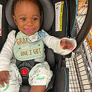 Dayton is registered to the contest to win money with this photo: baby, car_seat, shopping_cart, bib, smiling, child, grocery_store, clothing, person, seat_belt, infant, happy, indoor, aisle, retail, cart, food_products, pacifier, reaching_hand, cute
