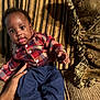 baby, child, plaid_shirt, navy_pants, socks, couch, cushion, striped_cushion, patterned_cushion, hand, indoor, portrait, smiling, curious, seated, person, furniture, home, cozy, textile