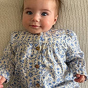 Esmee a rejoint le concours — aidez-le/la à gagner de superbes lots ! baby, child, infant, face, blue_eyes, dress, floral_pattern, buttons, hand, blanket, texture, portrait, cute, smile, lying_down, clothing, skin, hair, young, person