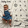baby, infant, denim_overalls, milestone_blanket, smiling, lying_down, wooden_floor, round_rug, numbers, months, white_blanket, text, cute, portrait, child, happy, indoors, clothing, hair, face