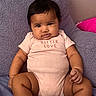 baby, infant, child, onesie, pink_clothing, socks, plush_cushion, purple_cushion, indoor, portrait, cute, chubby_cheeks, dark_hair, seated, looking_at_camera, skin, person, close_up, soft_texture, home