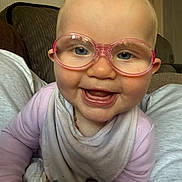 Laya-Mai joined the competition — help win amazing prizes! baby, glasses, smile, happy, face, indoor, clothing, bib, child, person, couch, furniture, head, eyes, mouth, skin, hair, portrait, cozy, infant