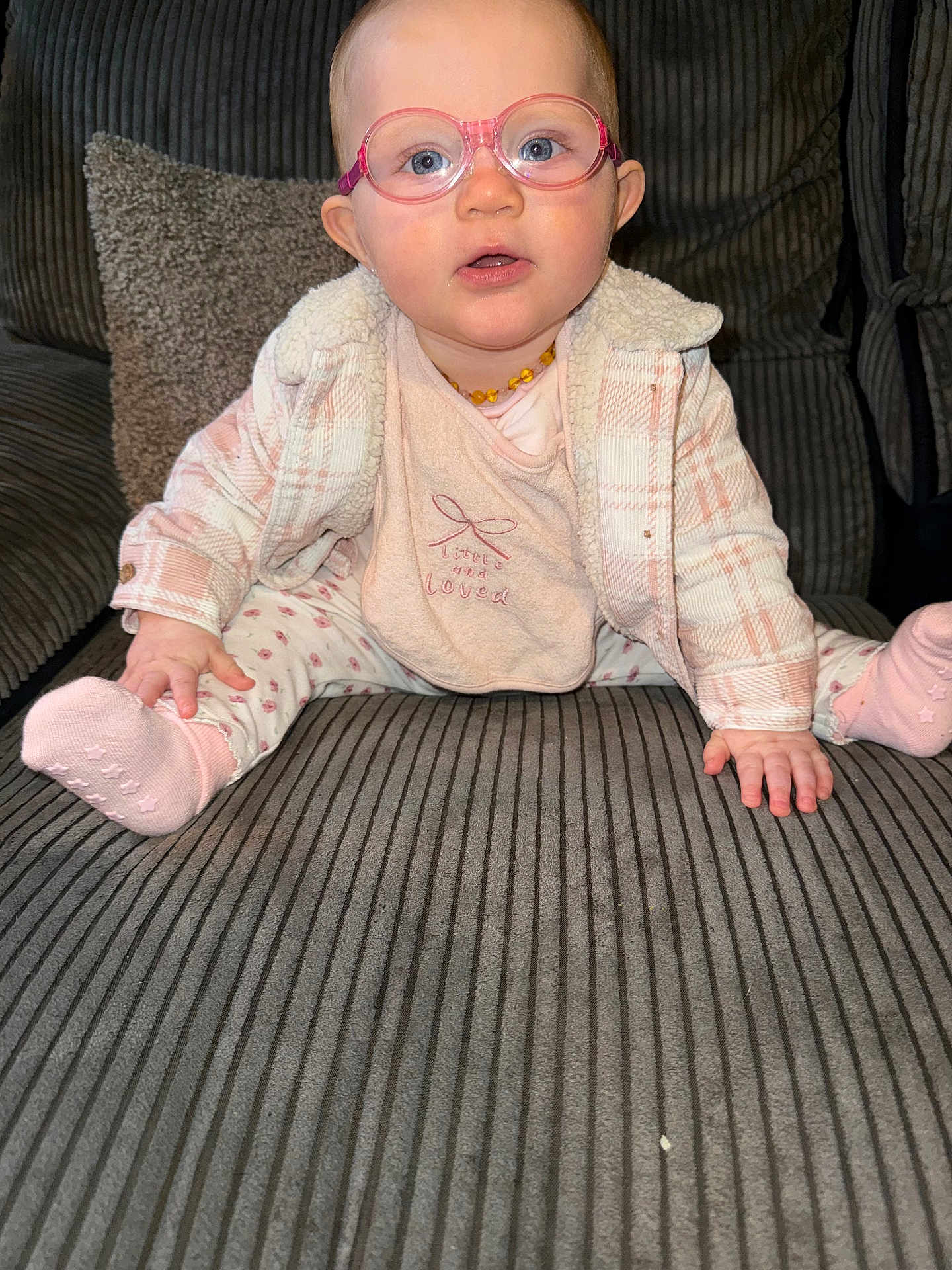 Laya-Mai joined the competition — help win amazing prizes! baby, child, glasses, pink, jacket, bib, socks, couch, plaid, seated, indoor, face, blue_eyes, hands, feet, portrait, cozy, cute, infant, furniture