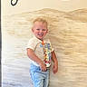 toddler, child, smiling, curly_hair, standing, tshirt, shorts, indoor, wall_art, blond, happy, casual_clothing, portrait, person, photo_screenshot, gallery_thumbnails, light_skin, background, text_partial, young_child