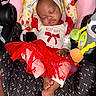 baby, sleeping, car_seat, headband, bow, dress, red, white, footwear, toy, plush_toy, infant, child, clothing, pattern, fabric, cute, peaceful, indoors, portrait