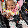 baby, infant, car_seat, headband, smile, child, clothing, floral_pattern, seatbelt, safety, cute, happy, portrait, indoors, person, pink, fabric, hand, eyes, head