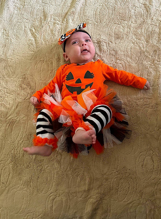 Emilee joined the competition — help win amazing prizes! baby, baby_toddler_clothing, carmine, child, face, flooring, fun, happy, hat, headwear, orange, pattern, person, personal_protective_equipment, sitting, sleeve, toddler