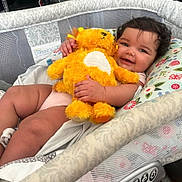 Octavia is registered to the contest to win money with this photo: baby, bassinet, stuffed_animal, smile, happy, infant, toy, fabric, cushion, child, cute, indoor, person, plush, comfort, rest, skin, hand, face, curly_hair