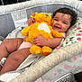 baby, bassinet, stuffed_animal, smile, happy, infant, toy, fabric, cushion, child, cute, indoor, person, plush, comfort, rest, skin, hand, face, curly_hair