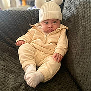 Khalil joined the competition — help win amazing prizes! baby, child, infant, hat, pom_poms, socks, clothing, sitting, couch, blanket, indoor, portrait, cute, cozy, soft_lighting, face, expression, person, home, warm