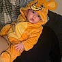baby, child, costume, lion, hood, orange, cute, infant, blanket, soft, indoor, person, face, eyes, hand, clothing, lying_down, expression, cozy, young