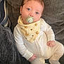 baby, infant, pacifier, onesie, bib, lion_pattern, blue_eyes, couch, gray_couch, soft_fabric, indoor, portrait, child, cute, looking_at_camera, relaxed, seated, close_up, young_child, comfortable