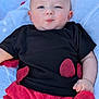 baby, infant, child, black_shirt, red_shorts, red_petals, blanket, outdoor, grass, cute, face, hand, skin, expression, lying_down, clothing, summer, casual, playful, portrait
