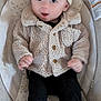 baby, infant, hat, jacket, clothing, seat, baby_seat, cushion, face, person, socks, black_pants, wood_floor, indoor, cute, child, portrait, warm_clothing, expression, smiling