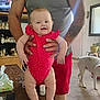 Arianna is registered to the contest to win money with this photo: baby, adult, red_onesie, polka_dot, table, dog, tattoos, television, woman, indoor, furniture, person, clothing, smiling, holding, legs, arms, face, living_room, household_items