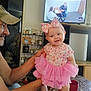 baby, cap, child, clothing, decor, family, foot, hand, happy, headband, indoors, living_room, man, person, pink, shelf, smile, table, television, tutu