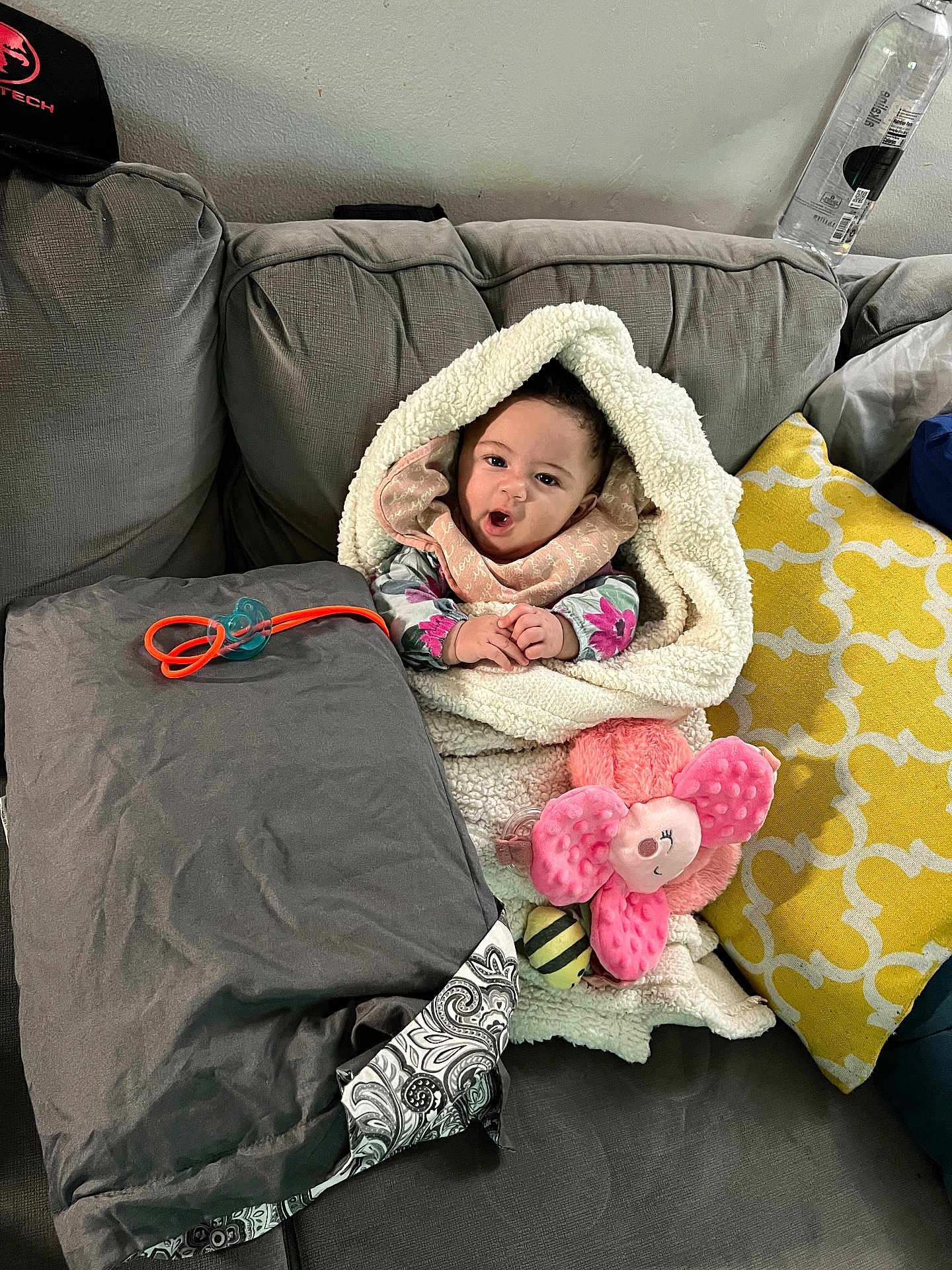 Sapphire joined the competition — help win amazing prizes! baby, blanket, couch, pillow, pacifier, plush_toy, child, face, expression, indoor, cozy, soft_toy, clothing, hand, seated, home, smiling, cute, wrapped, toy