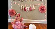 Tessa is registered to the contest to win money with this photo: child, toddler, baby, birthday, birthday_decorations, pink_dress, smiling, waving, sitting, indoors, party, paper_flowers, bunting, balloon, lantern, wooden_floor, wall, portrait, celebration, happy_birthday