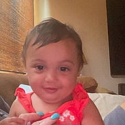 Tessa is registered to the contest to win money with this photo: baby, child, portrait, smiling, sitting, indoor, couch, home, window, blinds, coral_outfit, dress, turquoise_nails, hands, face, hair, eyes, warm_lighting, close_up, family_photo