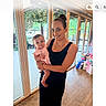 Tessa joined the competition — help win amazing prizes! baby, black_dress, casual, celebration, child, family, flooring, gift_bags, glass_doors, greenery, happy, holding, indoor, natural_light, person, pink_outfit, portrait, smile, window, woman