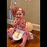 Tessa joined the competition — help win amazing prizes! baby, child, birthday, first_birthday, pink_dress, flower_headband, smiling, sitting, indoors, portrait, wood_floor, wall, decorations, paper_fan, lantern, number_one, birthday_outfit, barefoot, happy, celebration