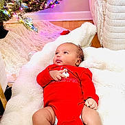 Amal is registered to the contest to win money with this photo: baby, infant, red_onesie, christmas_tree, christmas_lights, ornaments, holiday, festive, blanket, cozy, indoor, wood_floor, decorations, person, child, cute, celebration, happy, home, soft_texture