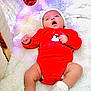 Amal joined the competition — help win amazing prizes! baby, infant, christmas, holiday, red_onesie, white_blanket, knit_hat, booties, ornament, decoration, festive, indoor, cute, lying_down, winter, celebration, soft_texture, cozy, happy, young_child