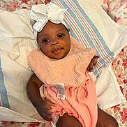 Ryleigh is registered to the contest to win money with this photo: baby, infant, child, smile, headband, bow, peach_outfit, blanket, bed, floral_pattern, striped_towel, cute, lying_down, indoors, person, skin, hand, face, happy, portrait