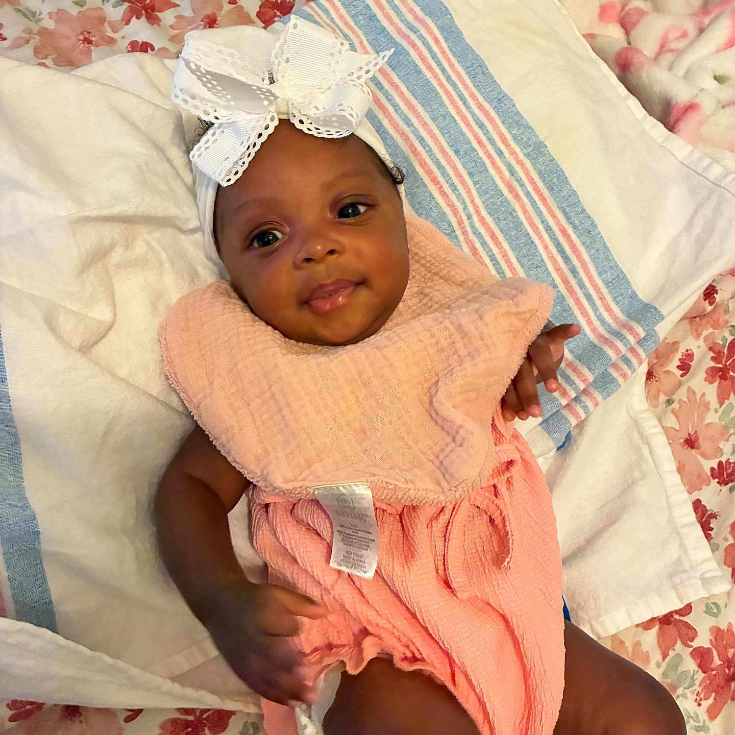 Ryleigh is registered to the contest to win money with this photo: baby, infant, child, smile, headband, bow, peach_outfit, blanket, bed, floral_pattern, striped_towel, cute, lying_down, indoors, person, skin, hand, face, happy, portrait