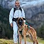 backpack, dog, forest, greenery, happy, harness, jacket, leash, mountain, nature, outdoors, path, person, pet_owner, portrait, rocky_path, sneakers, snow, standing, walking