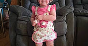 Mia is registered to the contest to win money with this photo: toddler, child, standing, hat, pink_clothing, shorts, shoes, socks, armchair, living_room, wood_floor, smiling, face, person, indoors, home, furniture, door, wall, cute