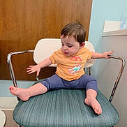 Mia joined the competition — help win amazing prizes! toddler, child, chair, orange_shirt, blue_pants, barefoot, indoor, waiting_room, floor, wood_panel, metal_armrest, curious, sitting, young_child, person, furniture, head, face, short_hair, casual_clothing