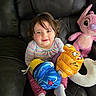 Mia is registered to the contest to win money with this photo: toddler, child, toy, boxing_gloves, plush_toy, pink_bunny, sofa, leather, sitting, happy, smiling, indoor, clothing, striped_shirt, pants, socks, cute, playful, young_child, face