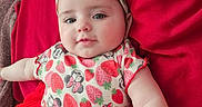 Mia is registered to the contest to win money with this photo: baby, child, closeup, clothing, cushion, cute, fabric, face, hand, happy, headband, indoor, infant, lying_down, person, portrait, red_tutu, skin, smiling, strawberry_pattern