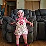 Mia is registered to the contest to win money with this photo: toddler, child, smiling, standing, indoor, armchair, clothing, hat, sneakers, wooden_floor, furniture, living_room, door, wall, happy, person, cute, pink, flower_pattern, home