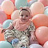 baby, child, balloons, pastel_colors, headband, bow, smiling, sitting, floral_pattern, bib, shoes, cute, happy, indoor, portrait, infant, playful, soft_colors, celebration, decor