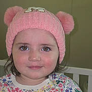 Mia is registered to the contest to win money with this photo: baby, child, clothing, cute, eyes, face, floral_shirt, girl, hat, headwear, indoors, innocent, knit_hat, person, pink_hat, pom_poms, portrait, smile, toddler, young_child